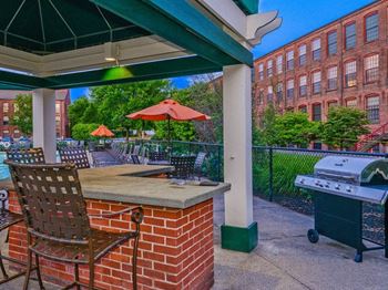a grill and chairs on a patio with a building in the background at Bigelow Commons, Enfield, CT, 06082